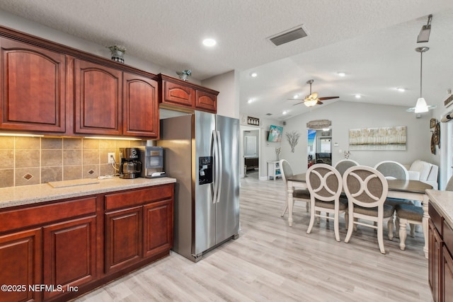 kitchen with decorative light fixtures, lofted ceiling, stainless steel fridge, decorative backsplash, and light wood-type flooring