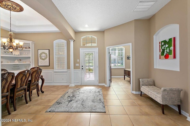 tiled foyer entrance featuring decorative columns, a notable chandelier, and a textured ceiling