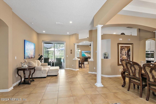 tiled living room featuring decorative columns and a textured ceiling