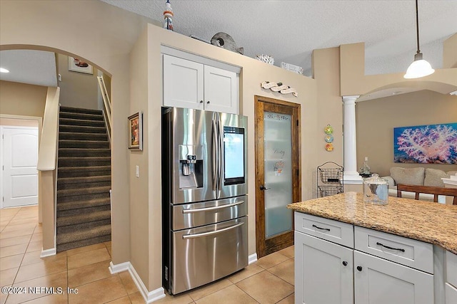 kitchen featuring light tile patterned floors, white cabinetry, stainless steel refrigerator with ice dispenser, light stone counters, and decorative light fixtures