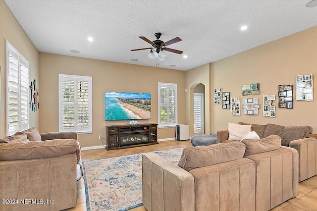 tiled living room with ceiling fan, a wealth of natural light, and a textured ceiling