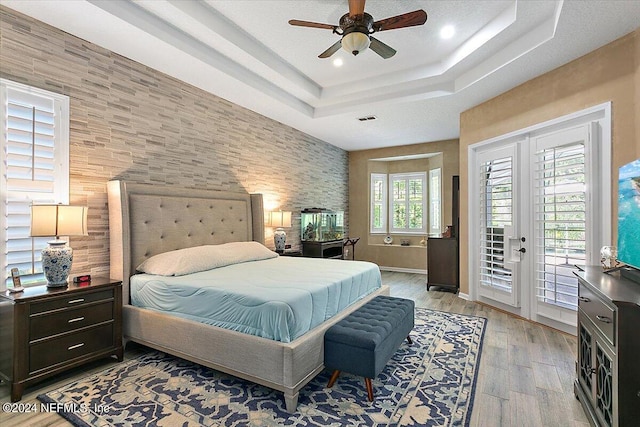 bedroom featuring light hardwood / wood-style flooring, access to outside, ceiling fan, a tray ceiling, and french doors