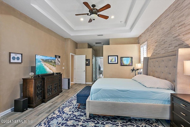 bedroom featuring a raised ceiling, ceiling fan, and light wood-type flooring