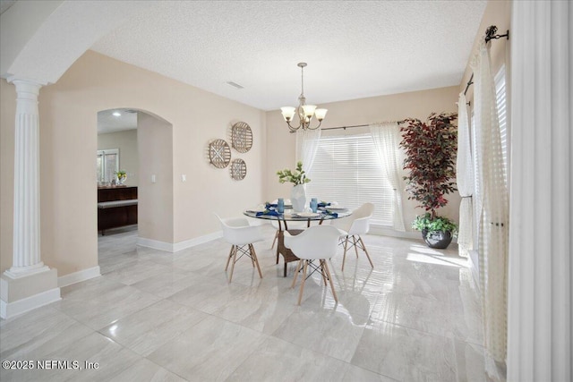 dining area featuring decorative columns, an inviting chandelier, and a textured ceiling