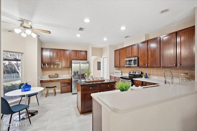 kitchen featuring sink, appliances with stainless steel finishes, a center island, decorative backsplash, and kitchen peninsula