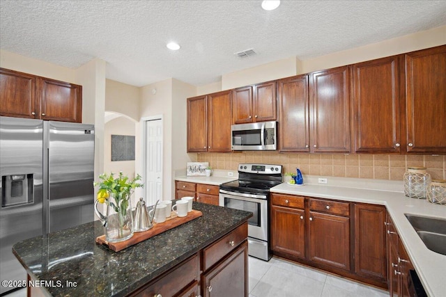 kitchen featuring tasteful backsplash, a textured ceiling, dark stone counters, light tile patterned floors, and stainless steel appliances