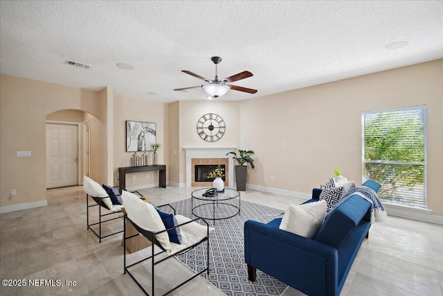 living room with a tiled fireplace, ceiling fan, and a textured ceiling