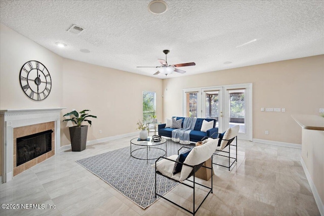 living room featuring french doors, ceiling fan, a tile fireplace, and a textured ceiling