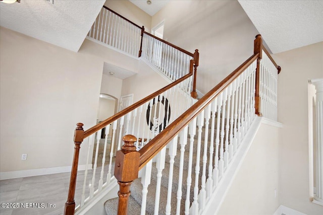 staircase with a towering ceiling and a textured ceiling