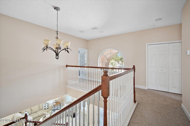 hallway featuring an inviting chandelier, carpet floors, and a textured ceiling