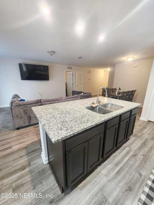 kitchen with open floor plan, light wood-style flooring, an island with sink, and a sink