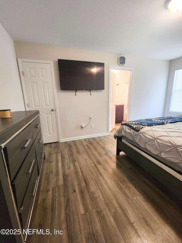 bedroom with connected bathroom, a textured ceiling, baseboards, and dark wood-style flooring