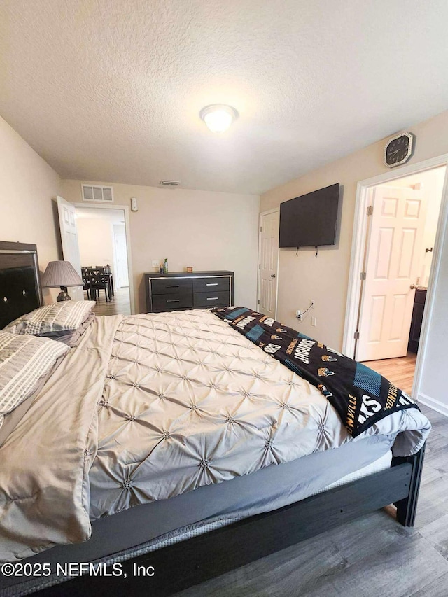 bedroom with visible vents, a textured ceiling, and wood finished floors