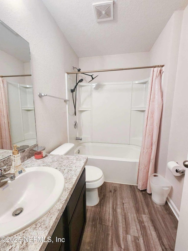 full bathroom featuring hardwood / wood-style flooring, vanity, shower / bath combination with curtain, a textured ceiling, and toilet