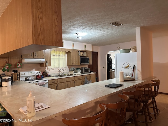 kitchen featuring white appliances, a breakfast bar area, kitchen peninsula, and a textured ceiling