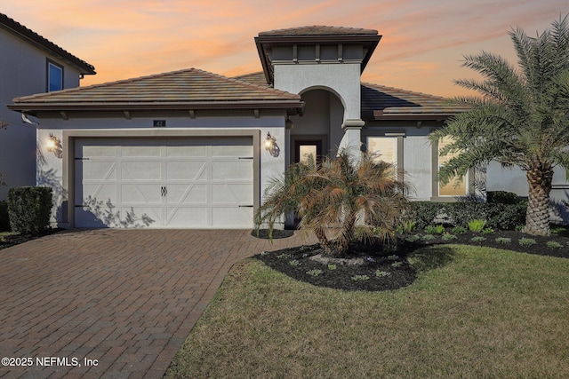 view of front of house featuring an attached garage, a tiled roof, decorative driveway, a lawn, and stucco siding