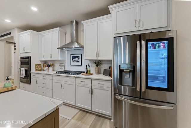 kitchen featuring stainless steel appliances, wall chimney range hood, and white cabinets