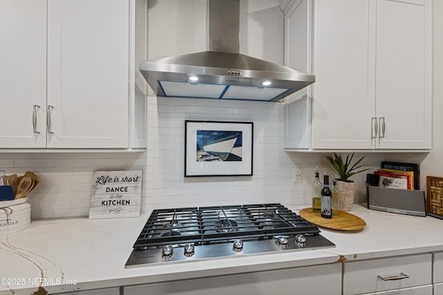 kitchen featuring light stone counters, white cabinets, stainless steel gas stovetop, and wall chimney range hood