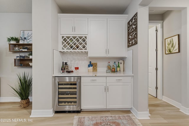 bar with backsplash, beverage cooler, light hardwood / wood-style floors, and white cabinets