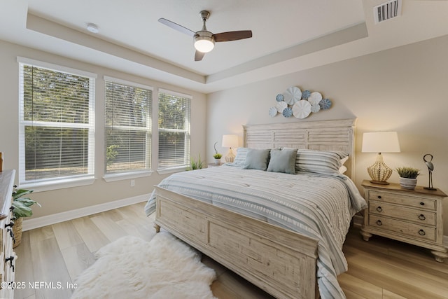 bedroom with a raised ceiling, ceiling fan, and light wood-type flooring