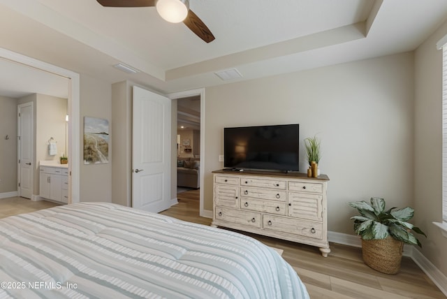 bedroom featuring a tray ceiling, ensuite bath, light hardwood / wood-style floors, and ceiling fan