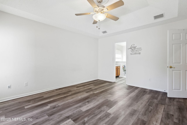 unfurnished room featuring a raised ceiling, dark wood-type flooring, and ceiling fan