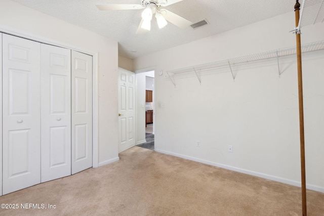 unfurnished bedroom featuring ceiling fan, light colored carpet, a textured ceiling, and a closet