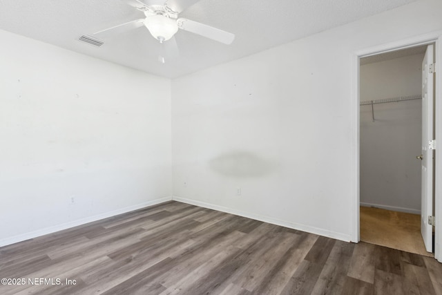 unfurnished bedroom featuring a walk in closet, wood-type flooring, a textured ceiling, a closet, and ceiling fan