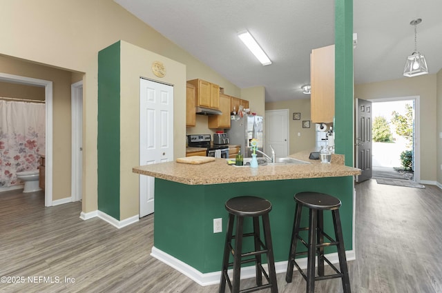 kitchen featuring sink, a kitchen bar, kitchen peninsula, stainless steel appliances, and light wood-type flooring