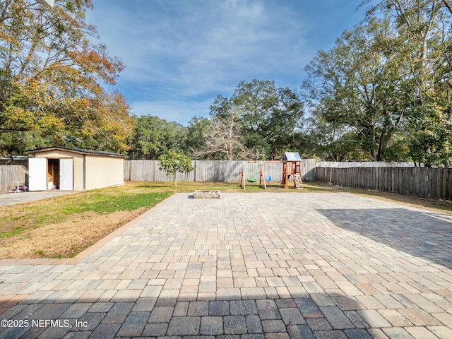 view of patio featuring a playground, a fire pit, and a storage unit