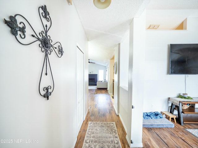 corridor with lofted ceiling, hardwood / wood-style floors, and a textured ceiling