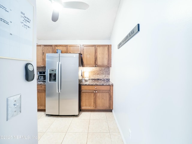 kitchen with light tile patterned floors, ceiling fan, stainless steel fridge with ice dispenser, decorative backsplash, and dark stone counters