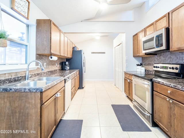 kitchen featuring lofted ceiling, sink, light tile patterned floors, appliances with stainless steel finishes, and decorative backsplash