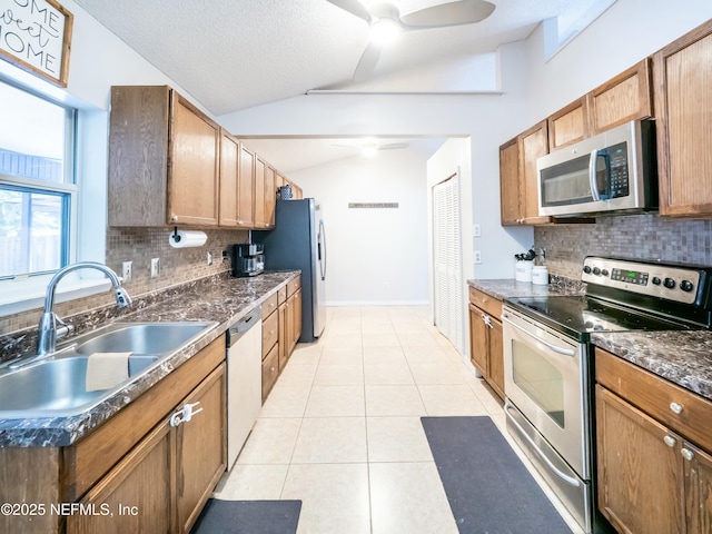 kitchen featuring sink, vaulted ceiling, light tile patterned floors, appliances with stainless steel finishes, and decorative backsplash