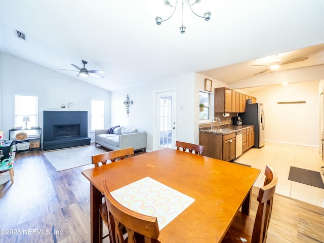 dining space featuring lofted ceiling, sink, ceiling fan, a fireplace, and light hardwood / wood-style floors