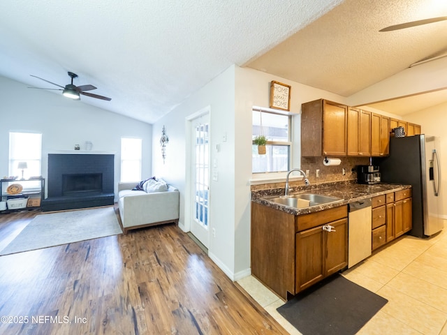 kitchen with sink, vaulted ceiling, a brick fireplace, and appliances with stainless steel finishes