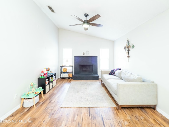 living room featuring lofted ceiling, hardwood / wood-style floors, a brick fireplace, and ceiling fan