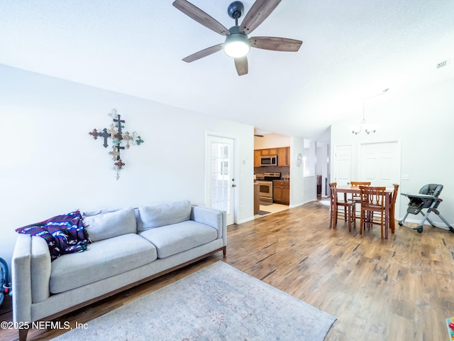 living room featuring ceiling fan with notable chandelier, vaulted ceiling, and light hardwood / wood-style floors