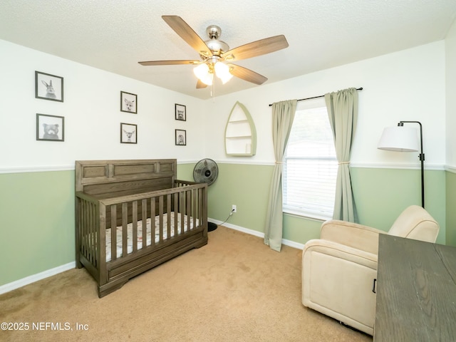 carpeted bedroom with ceiling fan, a nursery area, and a textured ceiling