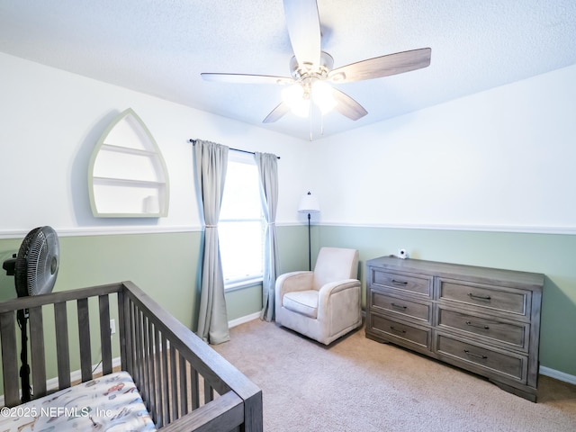 bedroom with a crib, light carpet, a textured ceiling, and ceiling fan