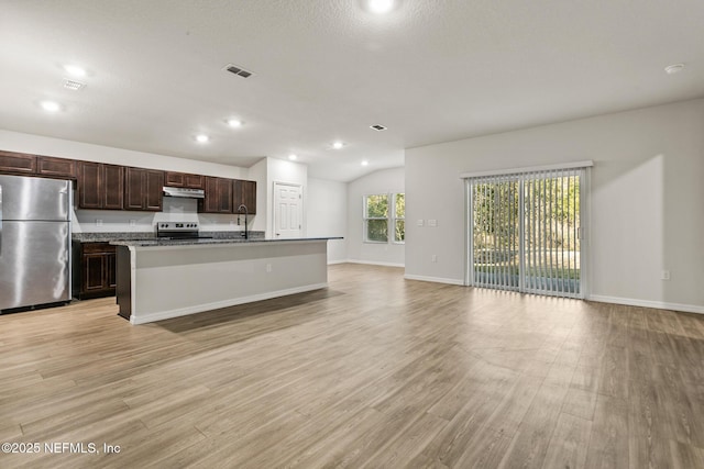 kitchen with light wood-type flooring, stainless steel appliances, a kitchen island with sink, and dark stone countertops