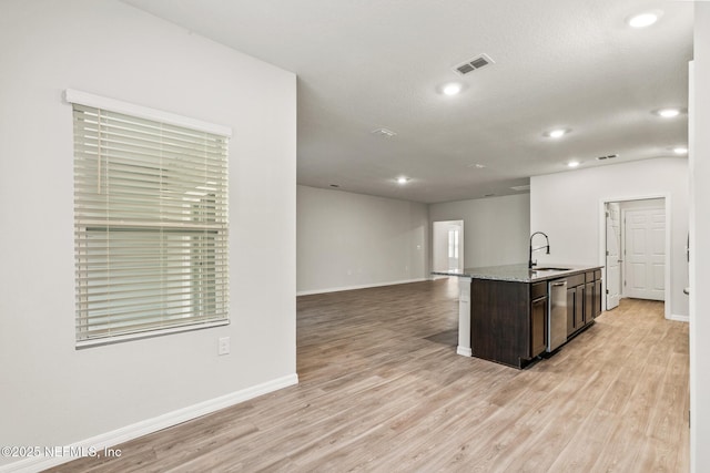 kitchen with sink, dark brown cabinetry, light hardwood / wood-style floors, light stone countertops, and a center island with sink