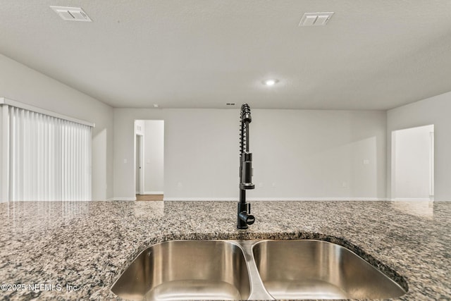 details with sink, a textured ceiling, and stone counters