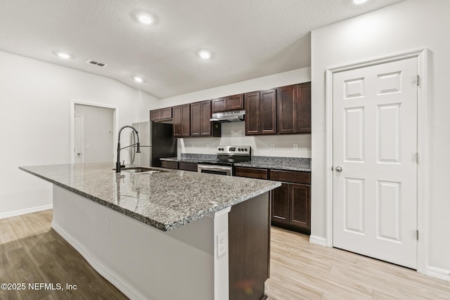 kitchen featuring light stone counters, dark brown cabinets, a center island with sink, light hardwood / wood-style flooring, and stainless steel appliances