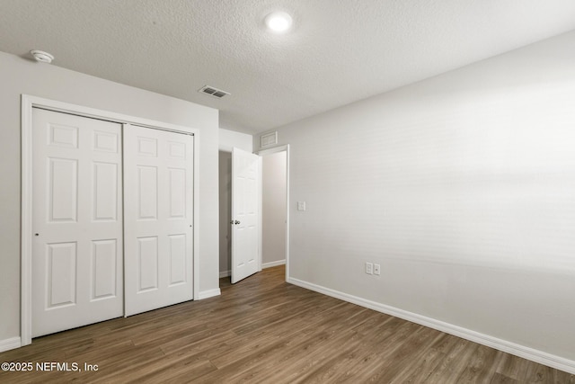 unfurnished bedroom with wood-type flooring, a textured ceiling, and a closet