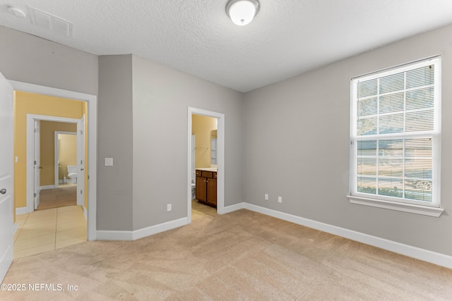 unfurnished bedroom featuring ensuite bath, light carpet, and a textured ceiling