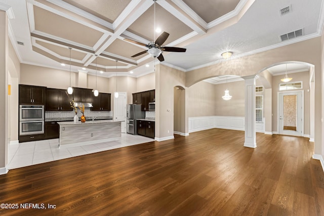 kitchen featuring hanging light fixtures, a towering ceiling, ceiling fan, stainless steel appliances, and a kitchen island with sink