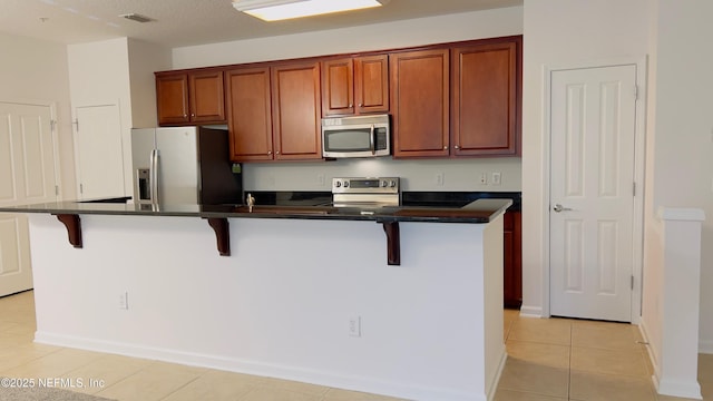 kitchen featuring light tile patterned flooring, appliances with stainless steel finishes, a kitchen island with sink, and a kitchen bar