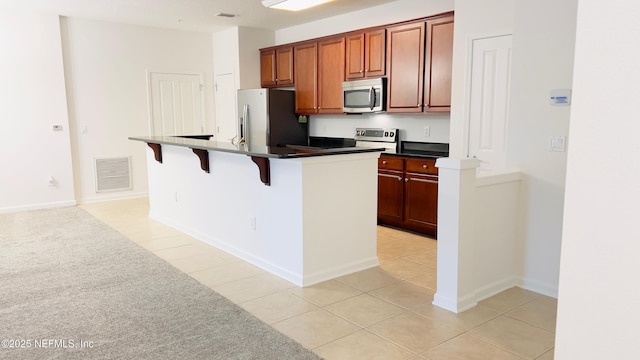 kitchen with a kitchen island with sink, light tile patterned floors, stainless steel appliances, and a kitchen bar