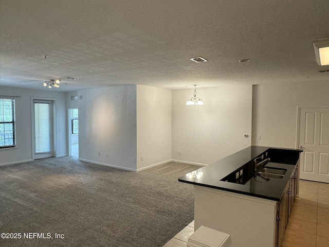 kitchen featuring sink, decorative light fixtures, a center island, a textured ceiling, and light colored carpet